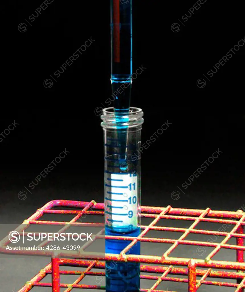 A pipette dispenses liquid into a test tube which is being held in a metal frame holder.