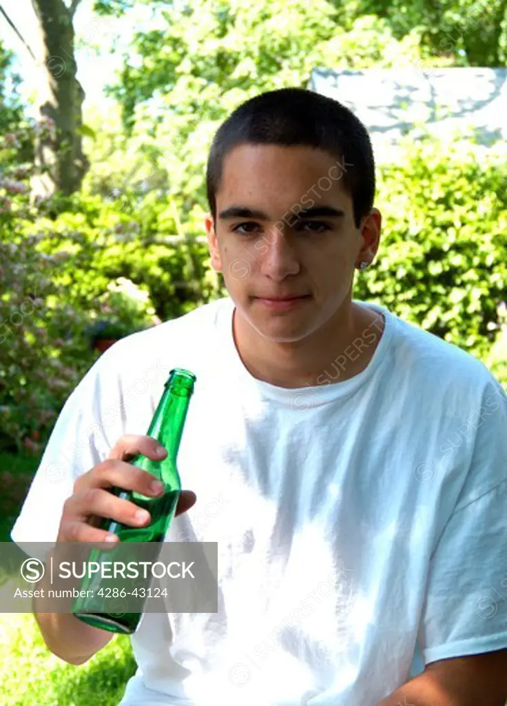 Teenage male holding an open beer bottle while outdoors. 