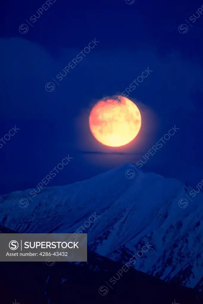 Full moon over snow-covered Alaska mountain range in Denali National Park, Alaska.