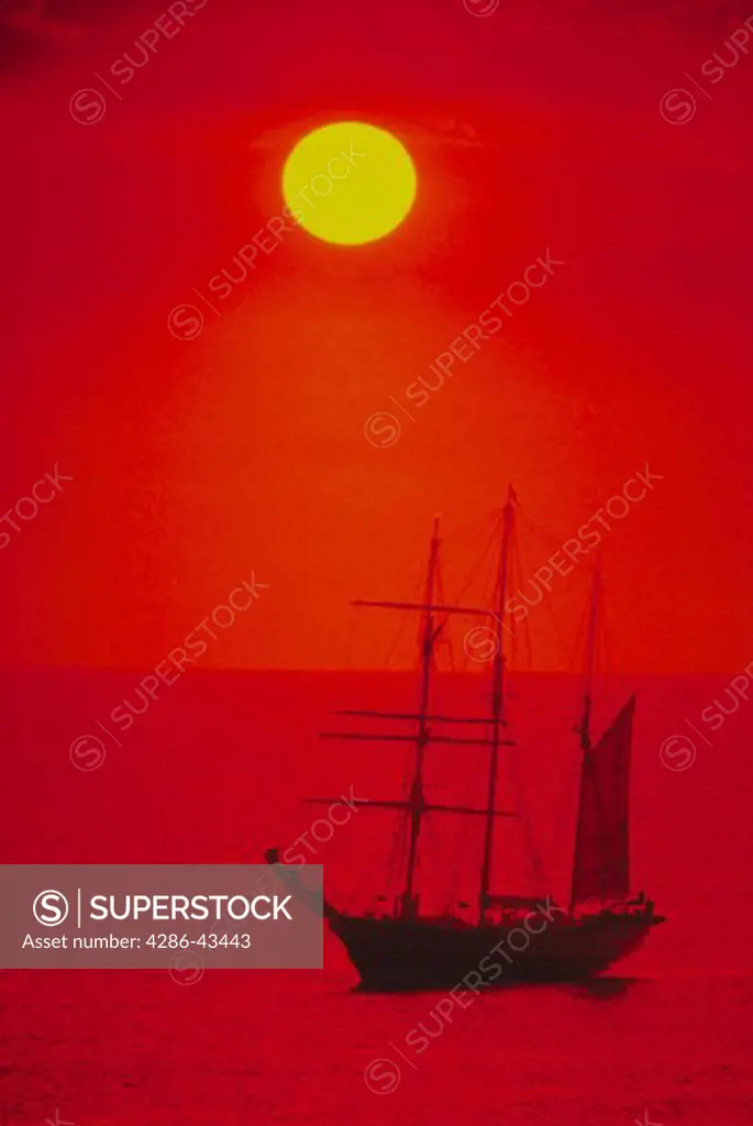 An orange sky and sun hang over a wooden schooner sailing off the coast of Western Australia.