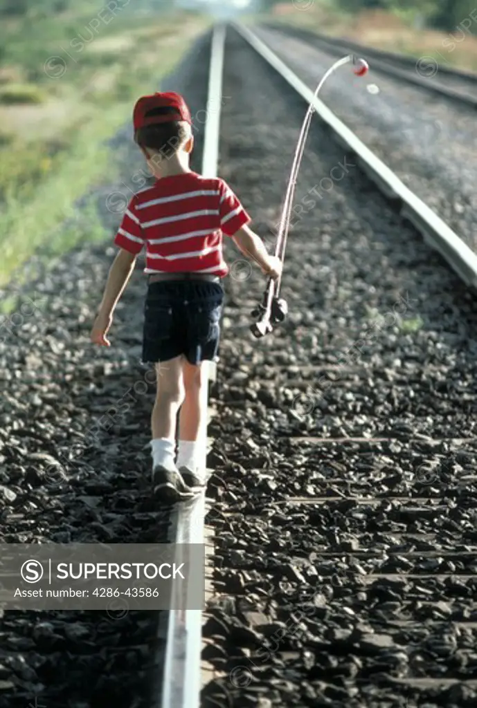 Boy walking on train tracks, with fishing pole, MR