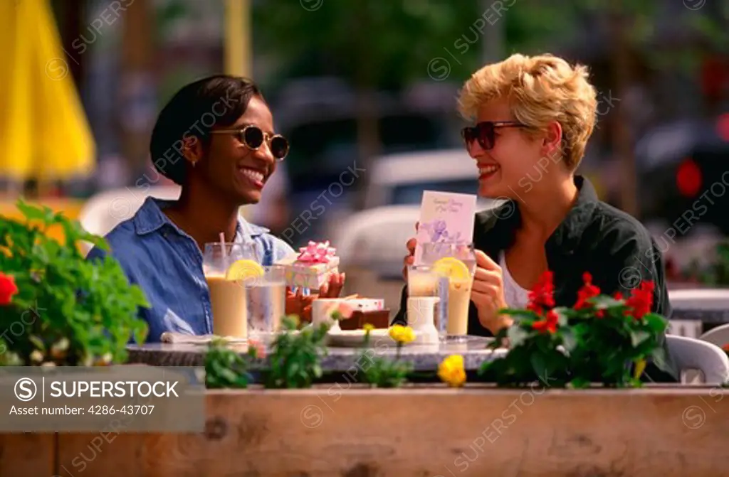 Two women eating lunch outside and exchanging a gift.