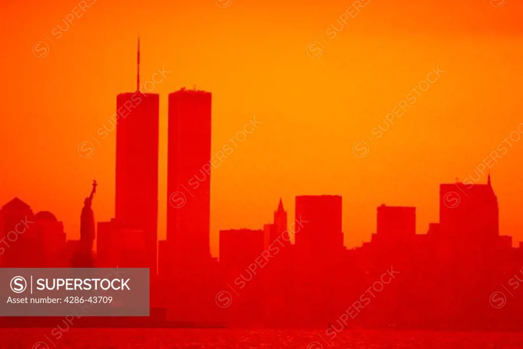 Silhouette of Statue of Liberty and New York City skyline against sunset.