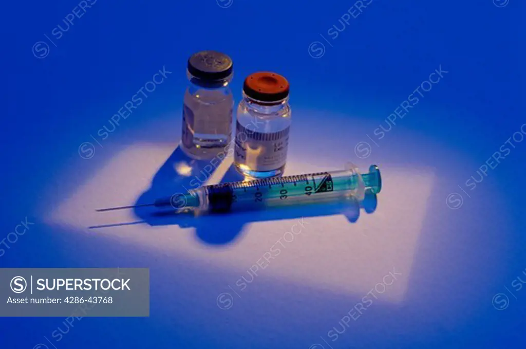 A spotlight shines on a hypodermic needle and two medicine bottles.