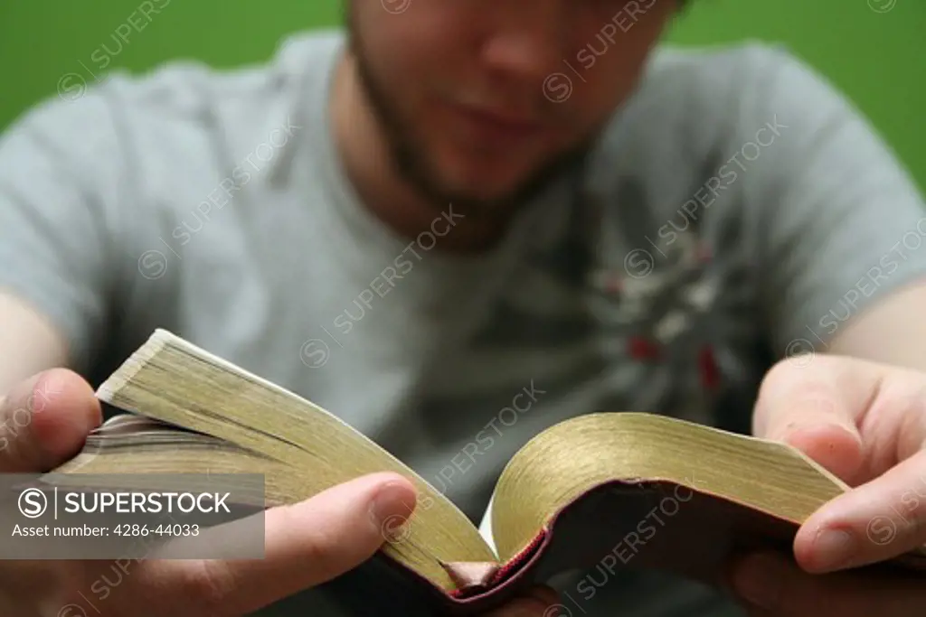 Young blond man reading the Bible with bright green background