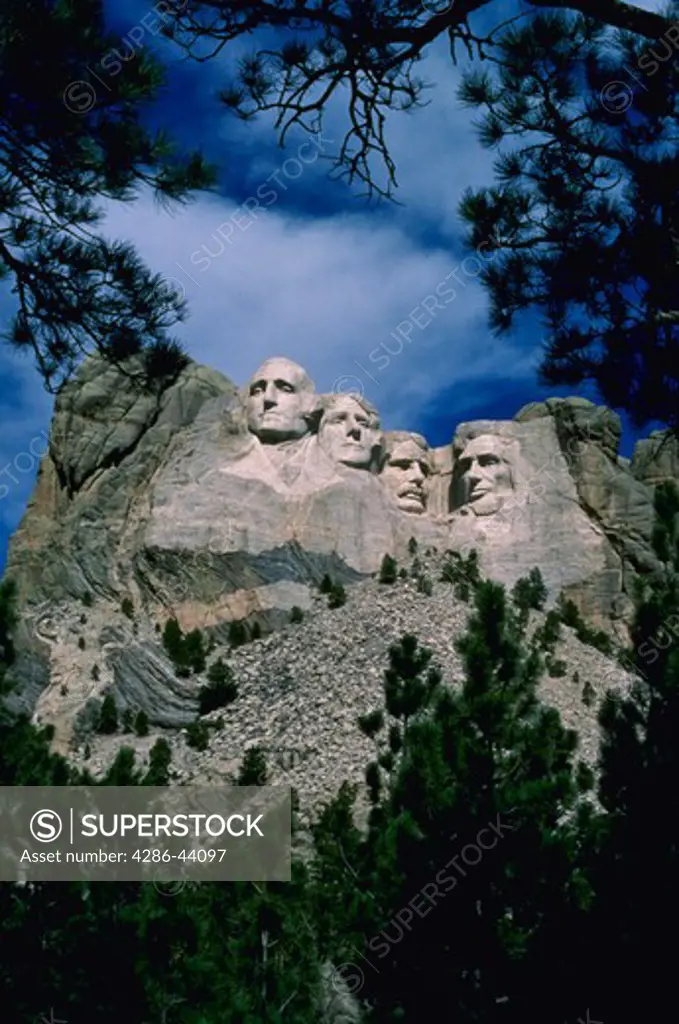 Mt. Rushmore National Memorial is framed by ponderosa pine trees.  The faces of presidents George Washington, Thomas Jefferson, Theodore Roosevelt, and Abraham Lincoln were carved on the granite peak by sculptor Gutzon Borglum.