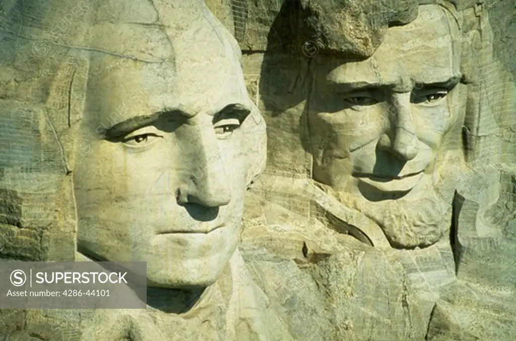 Aerial view of the granite faces of George Washington and Abraham Lincoln gazing out from the top of Mt. Rushmore National Memorial.  The faces of the other two presidents are hidden between them.