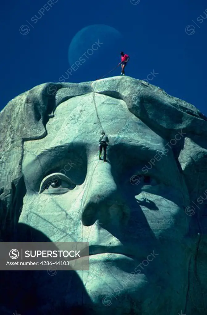 Geologists examine cracks in Thomas Jeffersons face at Mt. Rushmore as the moon sets behind the mountain.  (model released)