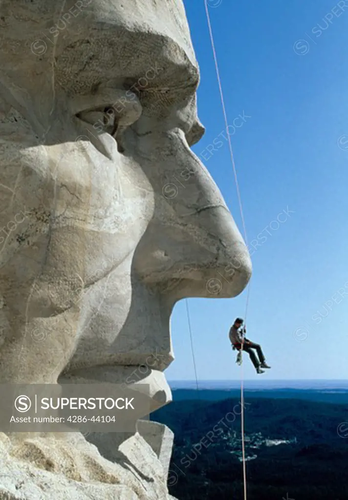 A national park service worker dangles beneath Abe Lincoln during an inspection of cracks at Mt. Rushmore.