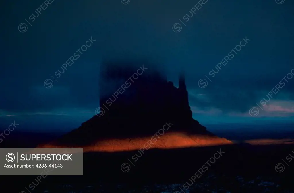  One of the Mitten Buttes is lit by a crack of light at sunset, beneath a deck of fog and clouds, at Monument Valley Tribal Park, in extreme northern Arizona.