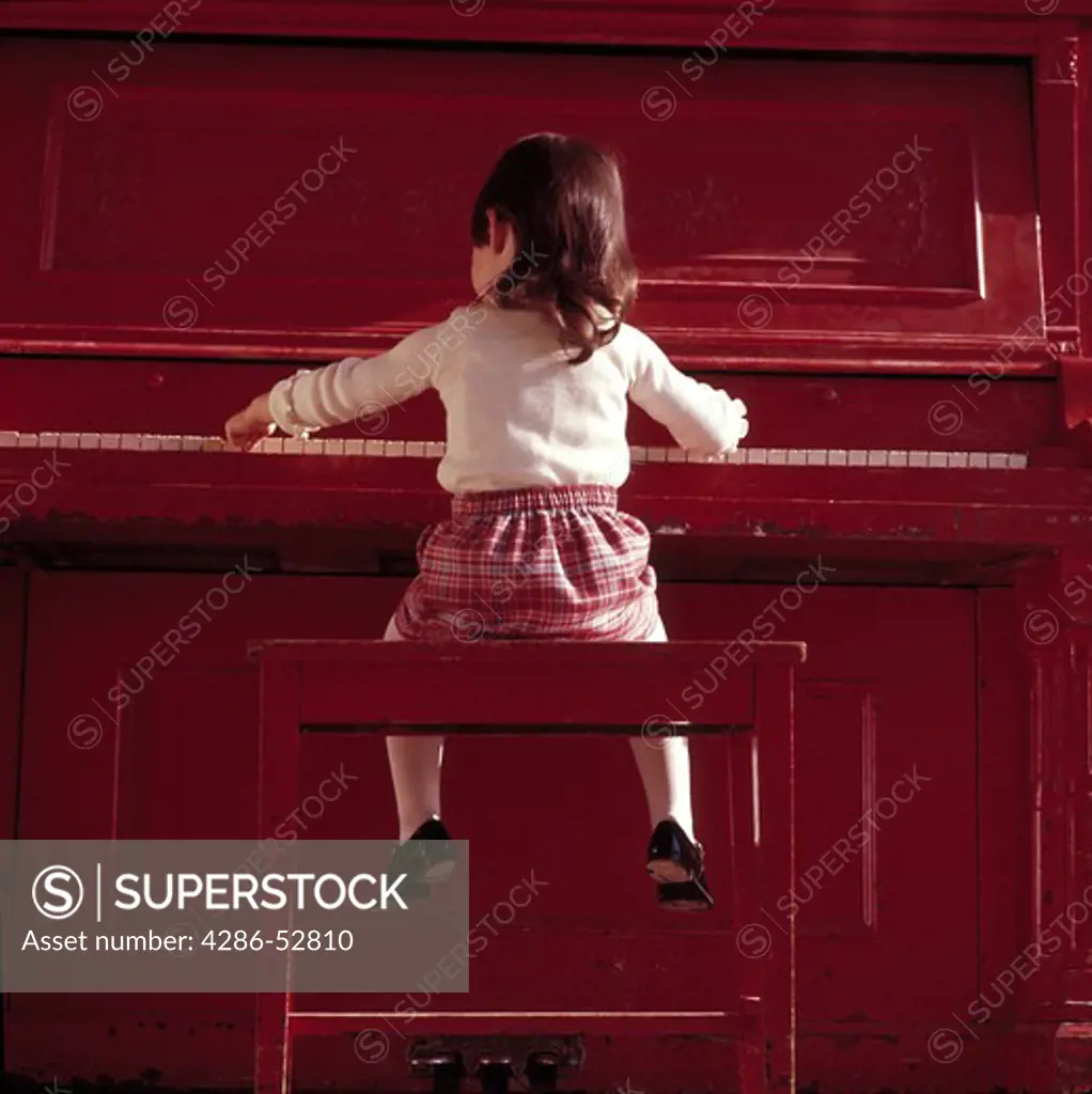 Young, little girl playing the piano as her feet dangle in the air.