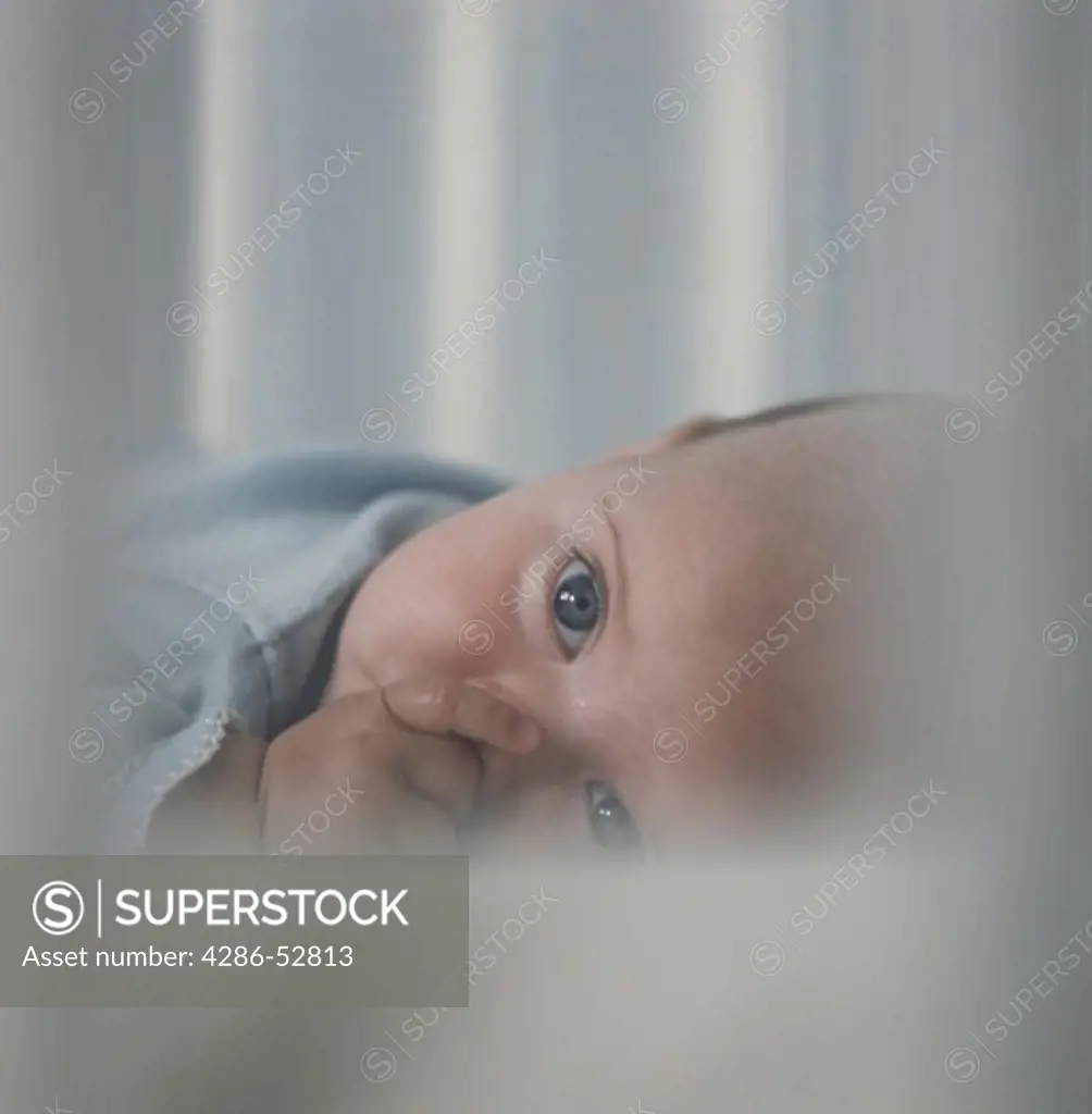 Up-close of an infant lying in a crib while sucking its thumb.