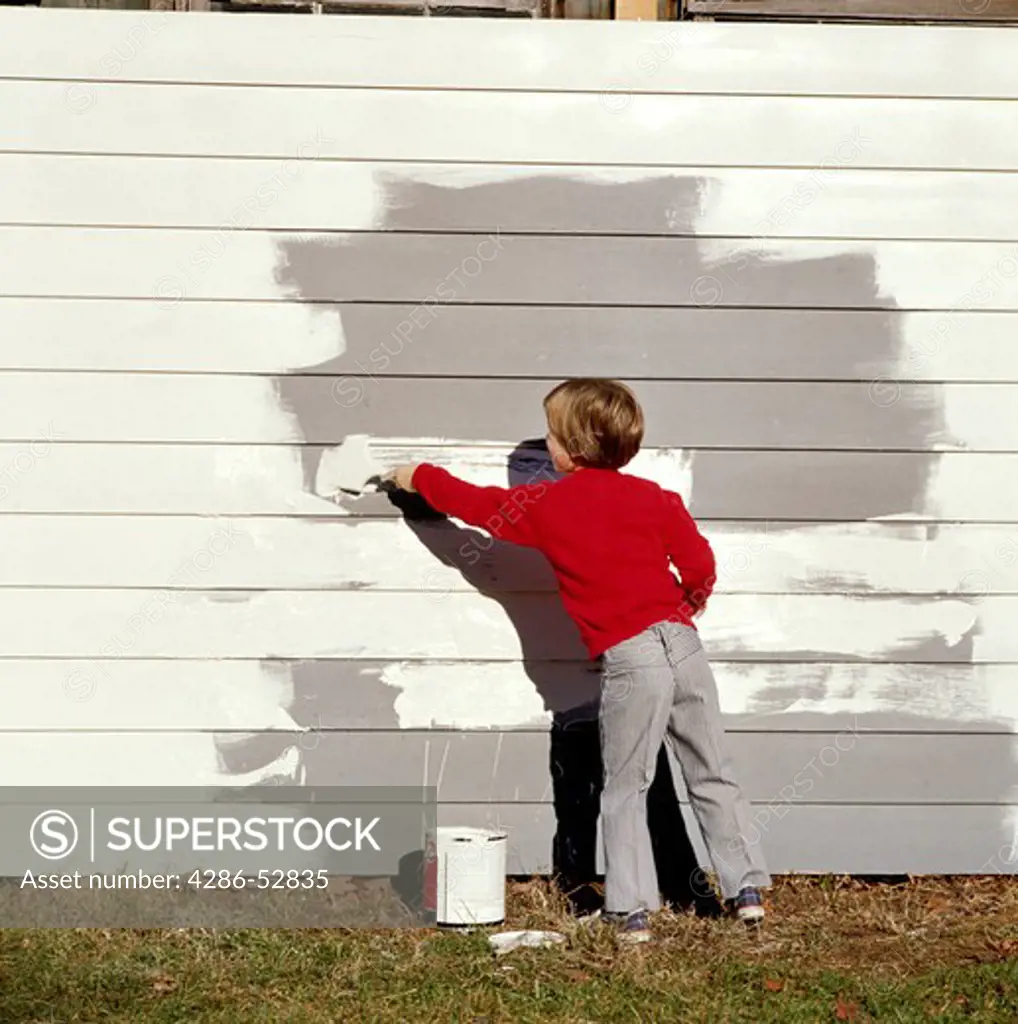 Young boy painting from side to side the exterior of a white wall.