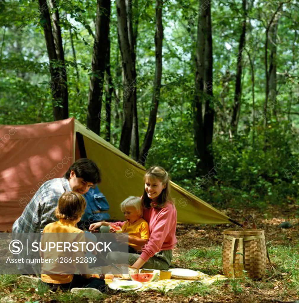 Father, mother and two children having a picnic in their campsite outside their tent. 