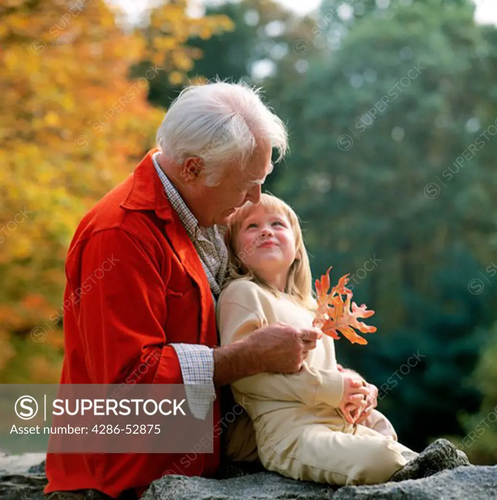 A grandfather showing his granddaughter some fall leaves as she looks up at him adoringly.