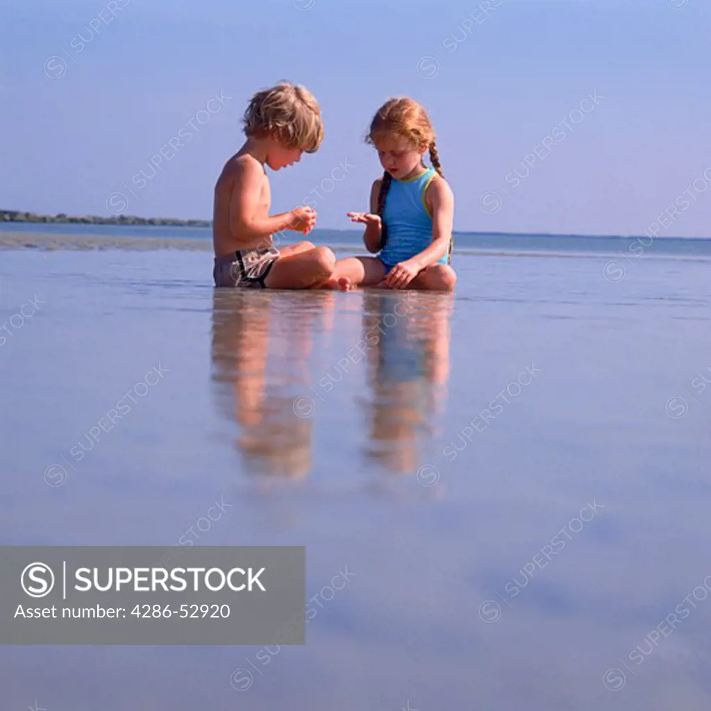 A young boy and young girl sitting together in a tidal pool at the beach.