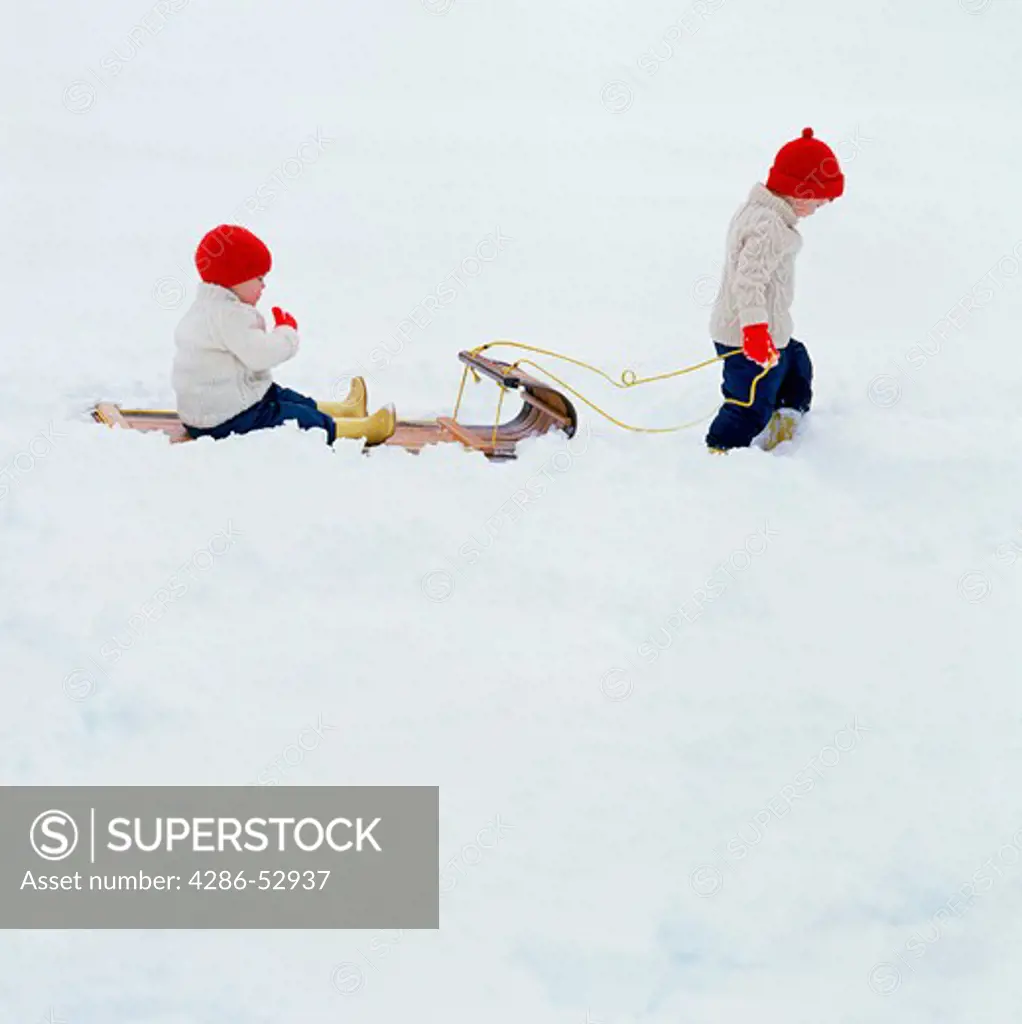 A young child pulling another child on a toboggan type sled through the snow.