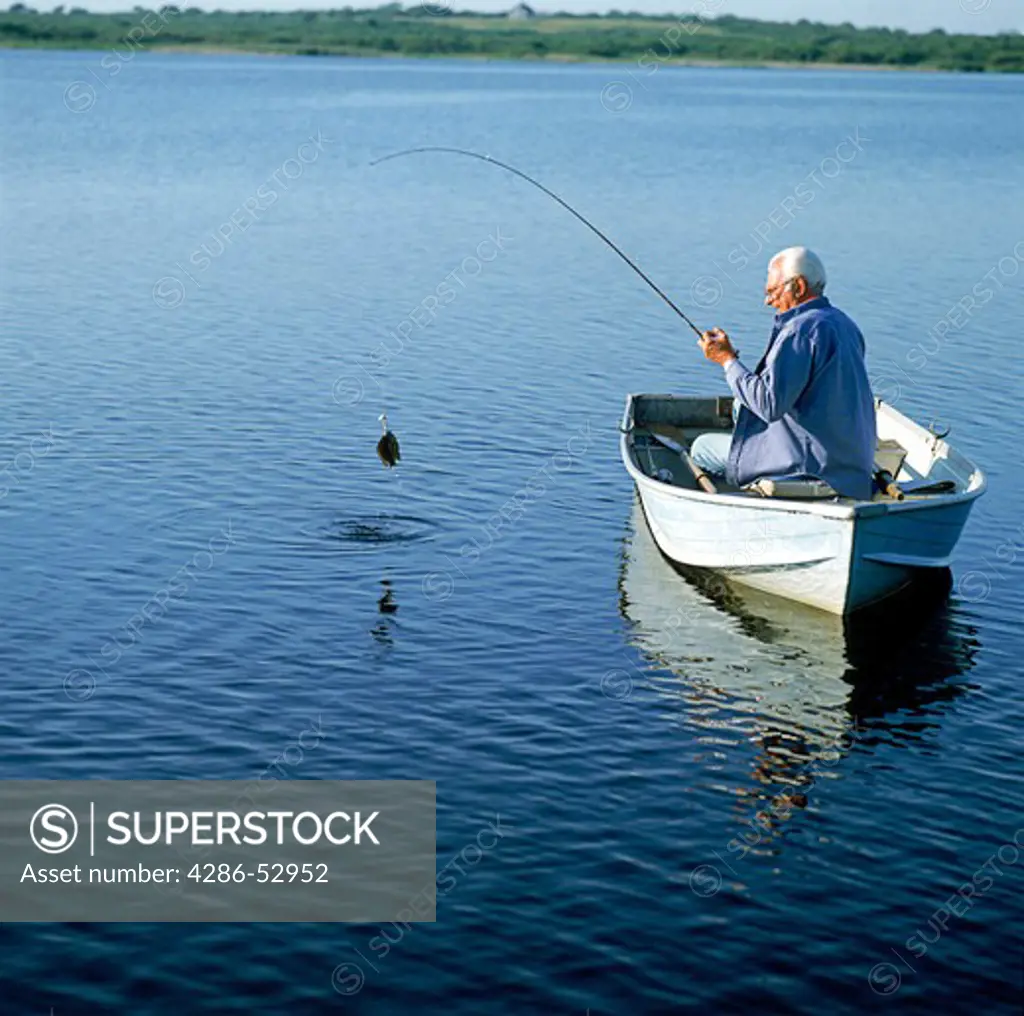 A senior man in a row boat reels in his catch.