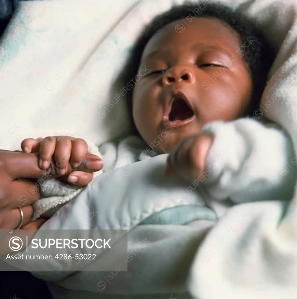 Close-up of an African-American baby wrapped in a blue blanket yawning. 
