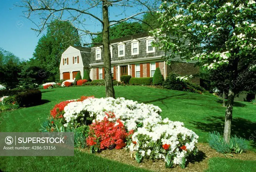 Red and white flowers in foreground of exterior view of front of brick house with cedar shake shingles. Property released.