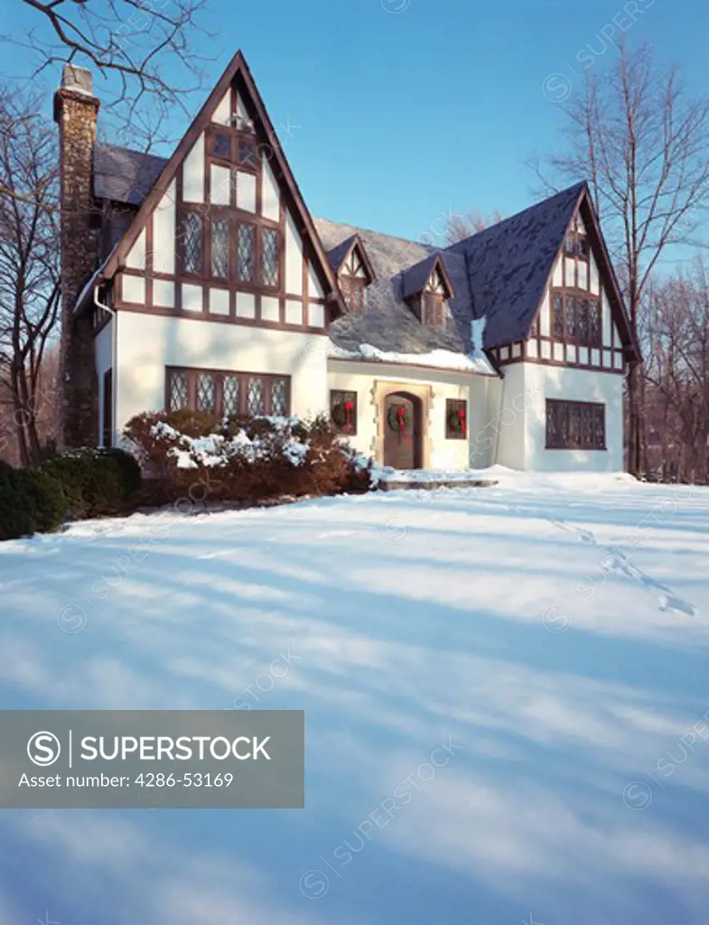 Exterior view of multi-story Tudor style house on a snowy day decorated with wreaths and red ribbons. Property released.