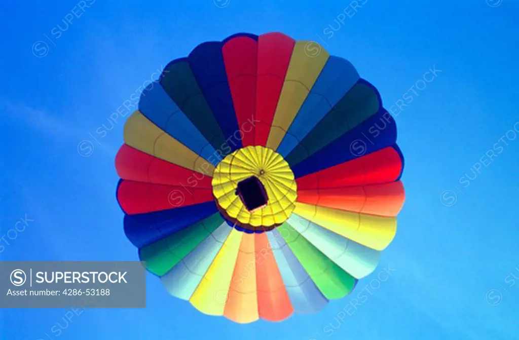 A colorful hot air balloon rises serenely directly overhead into the blue sky.