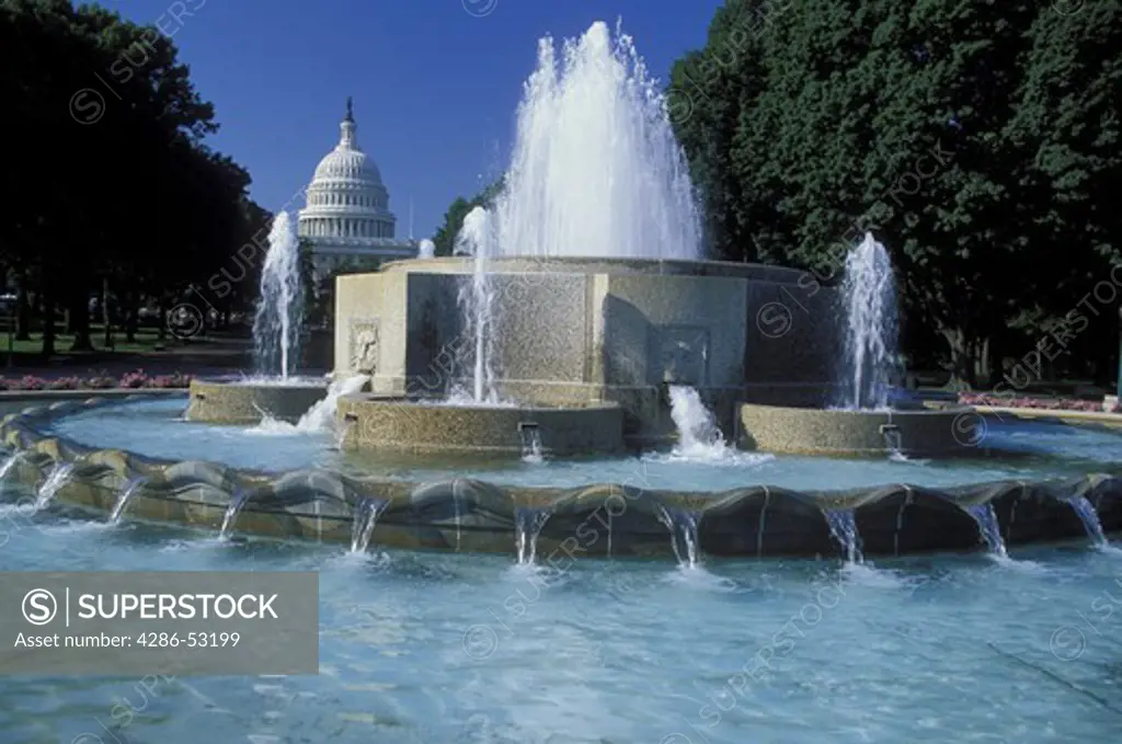 A decorative fountain sprays water while the dome of the U.S. Capitol rises behind it on a sunny day.