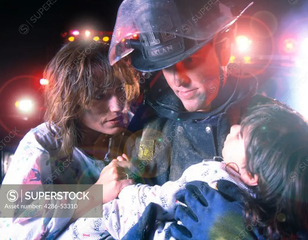 Fireman holding child, with mother looking on.