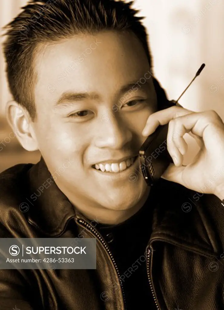 Close-up of an Asian man smiling while talking on a cellular phone.