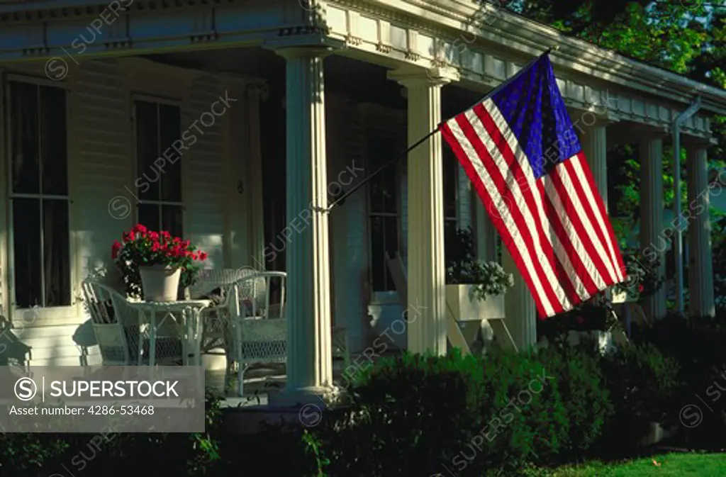 Traditional front porch of a house with an American flag hanging from the post, Newfame, Vermont.  Property released.