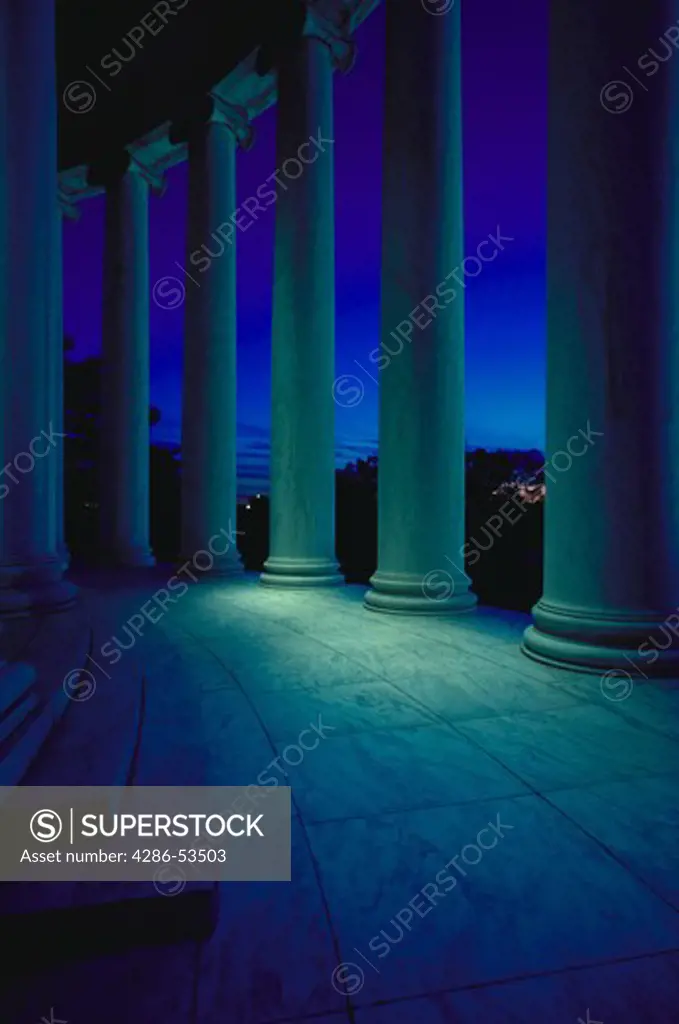 Marble columns in circular formation around building at night, with night lighting.