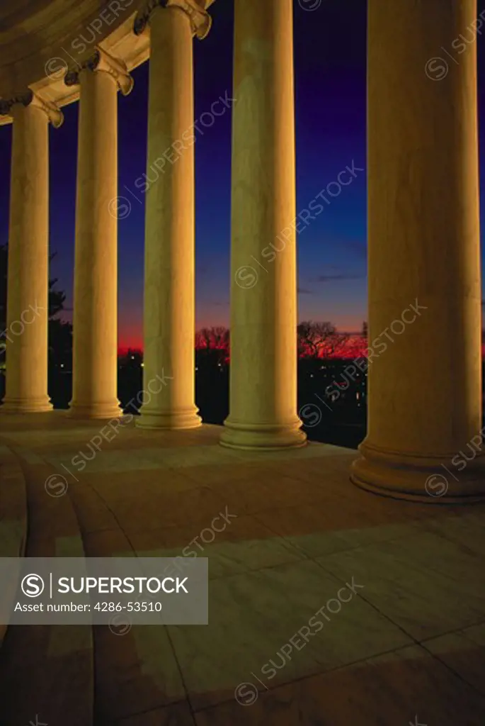 Marble columns in circular formation around building at night, with night lighting.