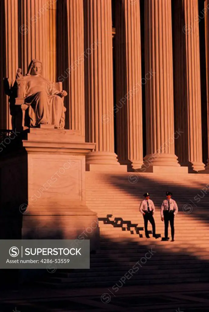 Two uniformed policemen standing on the steps of U.S. Supreme Court building in the light of a sunset, Washington D.C.