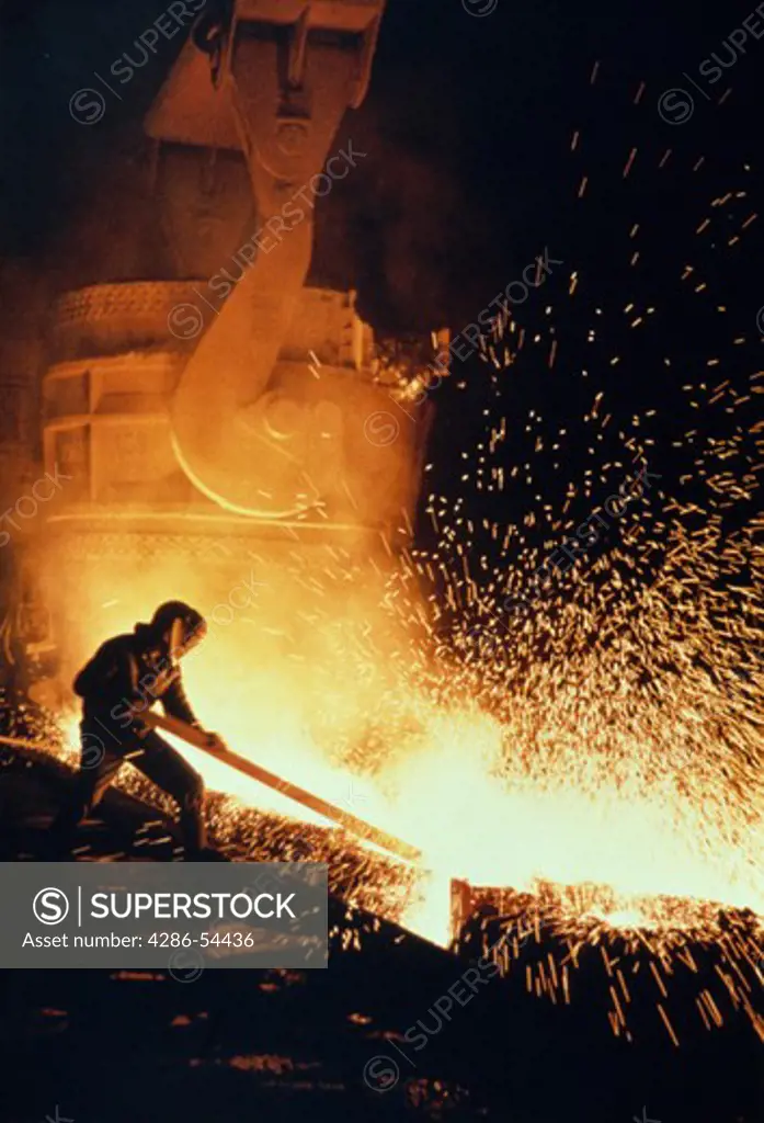 Silhouette of steel worker in steel mill against flaming sparks of molten steel.