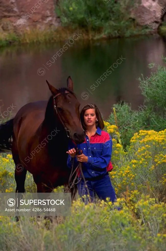 Female model with horse in scene with pond in background and yellow bushes in foreground.
