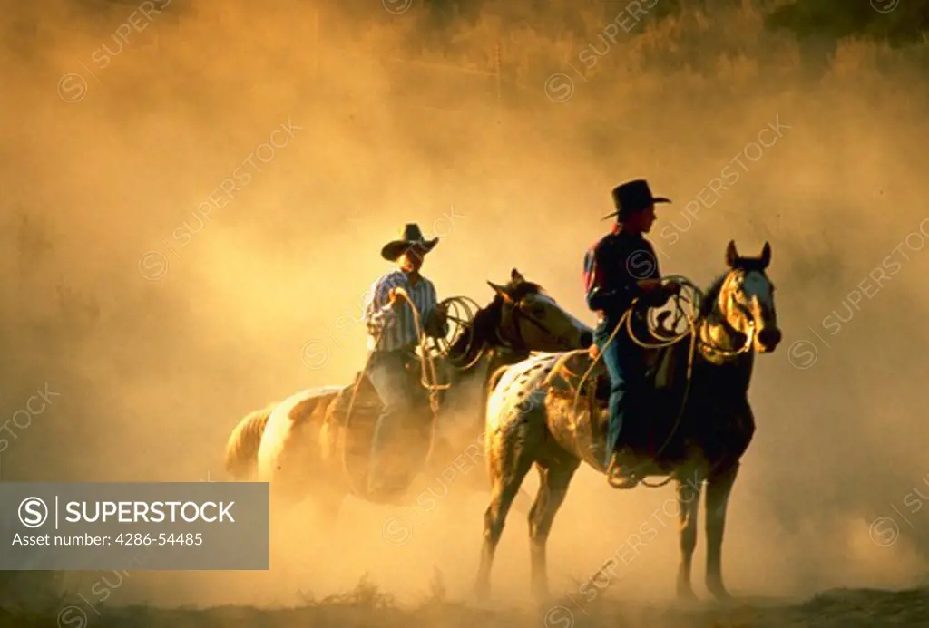 Two wranglers/cowboys on horseback in a dusty scene