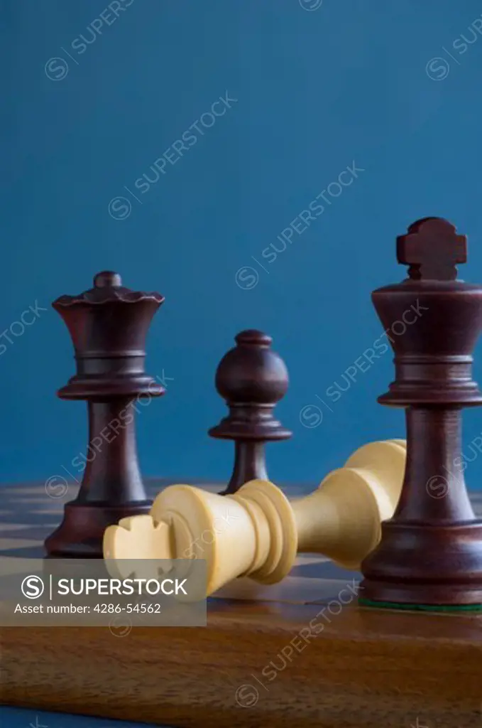 A close-up of four chess pieces set a top a wood chess board with one of the pieces laying on its side.