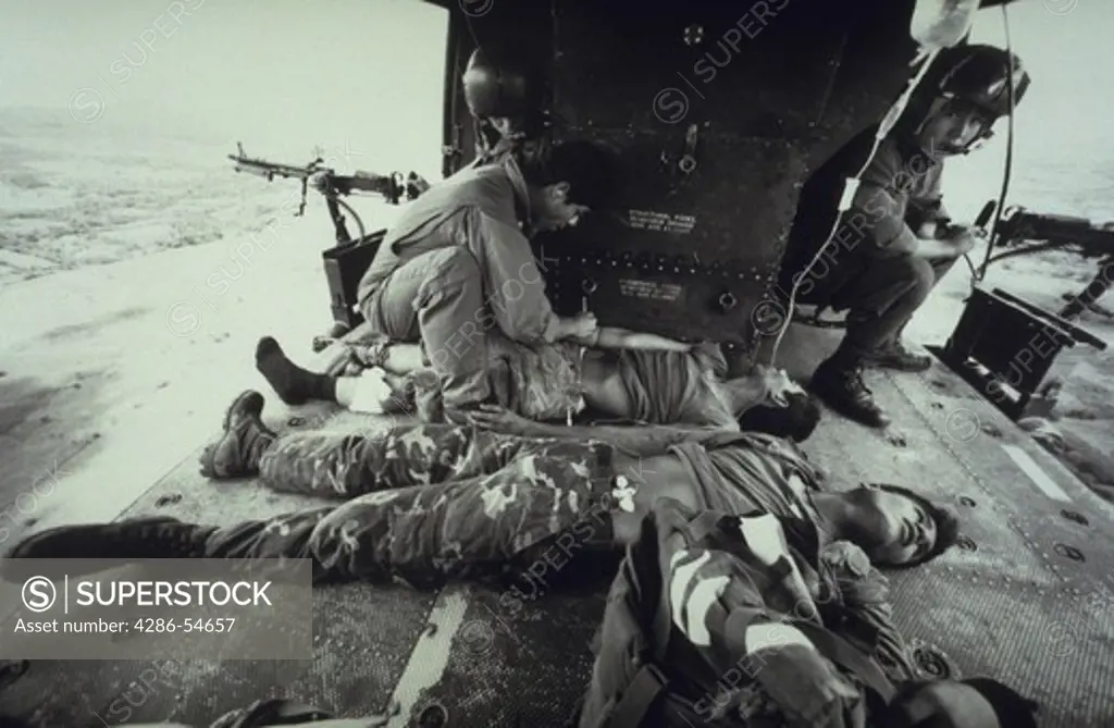 Salvadoran medic tends to wounded soldiers as door gunners watch.  Picture is one of a series documenting a helicopter squadron in El Salvador during the war.