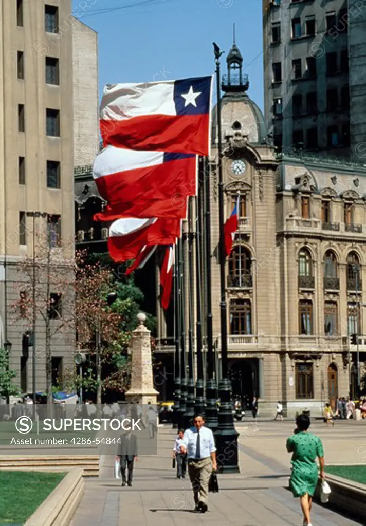 As Chile's flag flies over head, pedestrians stroll through Constitution Plaza, near 'La Moneda' (Presidential Palace) in downtown Santiago, Chile.