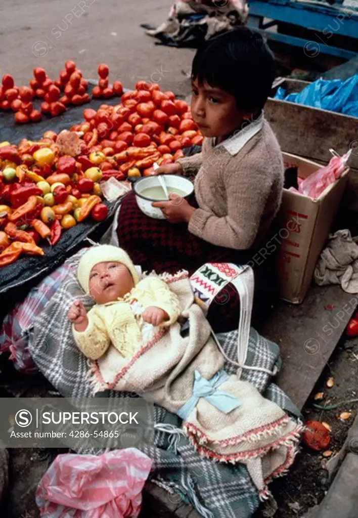 Young boy eats soup for breakfast at his mothers street vending stand, as he watches over his infant cousin in the city of Huancayo, Junin Department, Peru.