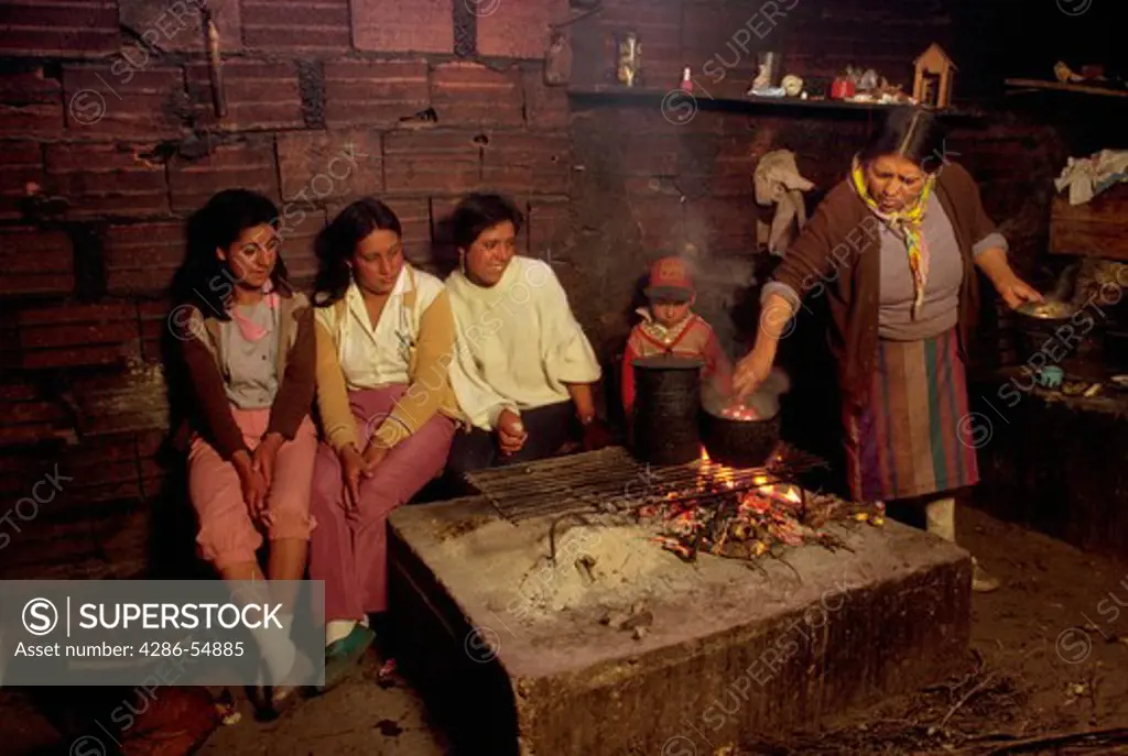 Woman cooks over a crude indoor fire as young girls look on near Casa de Gobierno, Merida State, in the Venezuelan Andes.