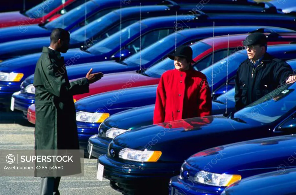 Salesman and two customers with new 1994 Ford Taurus automobiles in outdoor lot at Crystal Ford in Silver Spring, Maryland.