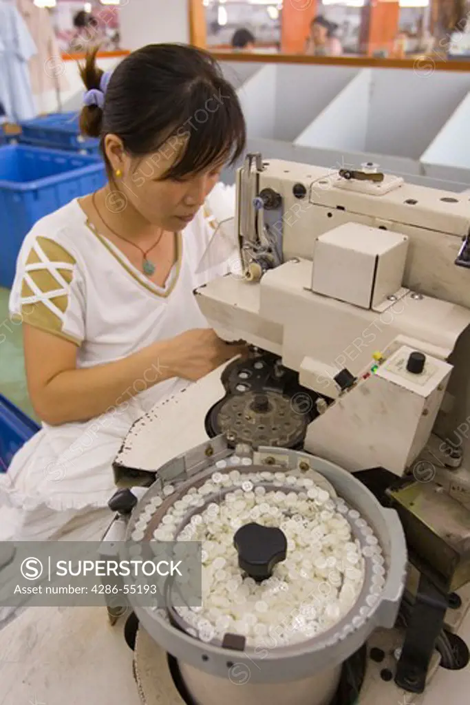 SHENZHEN, GUANGDONG PROVINCE, CHINA - Woman operates button machine, in garment factory in city of Shenzhen, one of mainland China's first Special Economic Zones, SEZ.