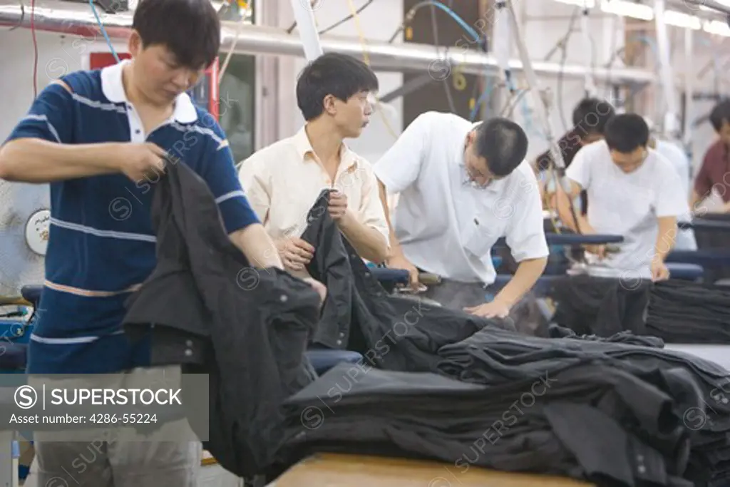 SHENZHEN, GUANGDONG PROVINCE, CHINA - Men ironing finished clothing, in a garment factory in city of Shenzhen, one of mainland China's first Special Economic Zones, SEZ.