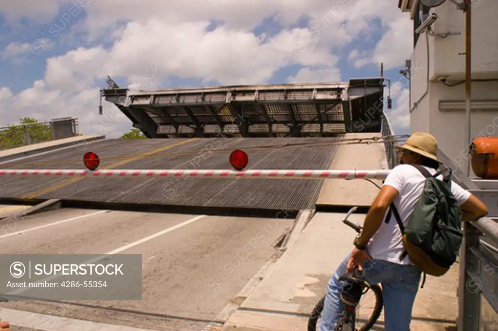 MIAMI, FLORIDA, USA - Draw bridge opens over Miami RIver as man on bicycle watches.