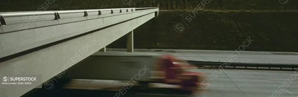 Blurred image of an 18-wheeler truck passing by an underpass on an interstate. 