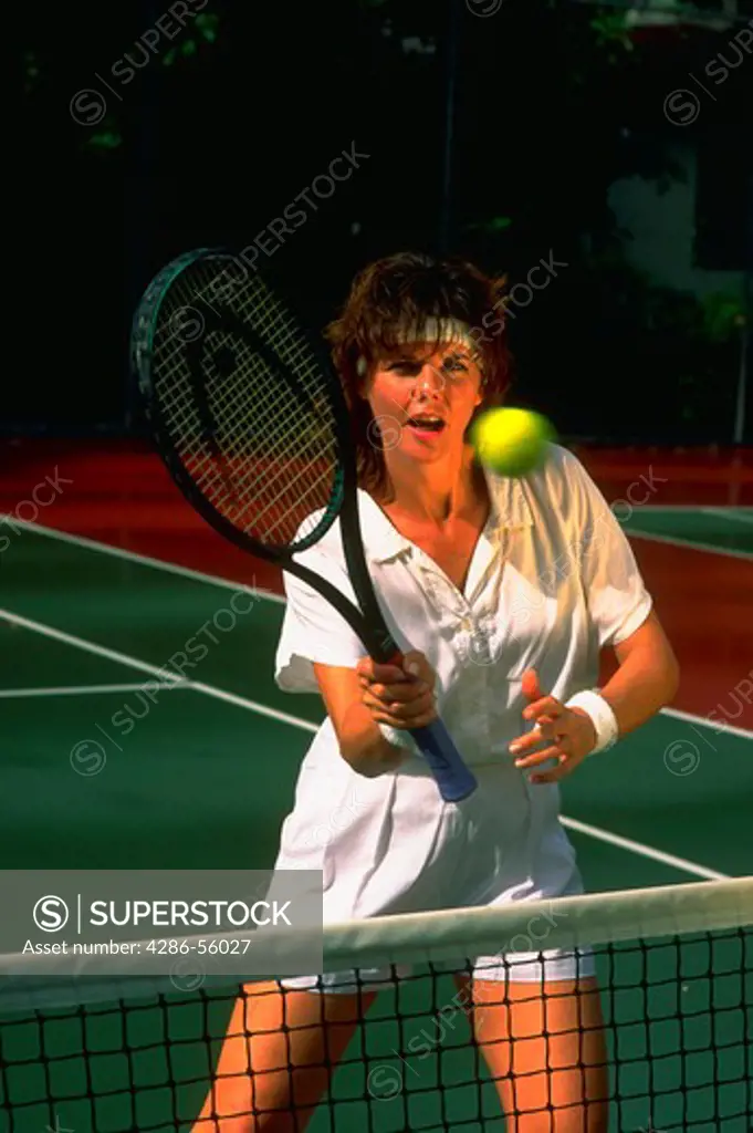 Woman hitting tennis ball at the net.