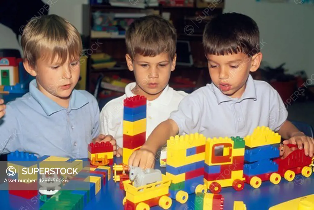 Three young boys playing with large Lego blocks at school.