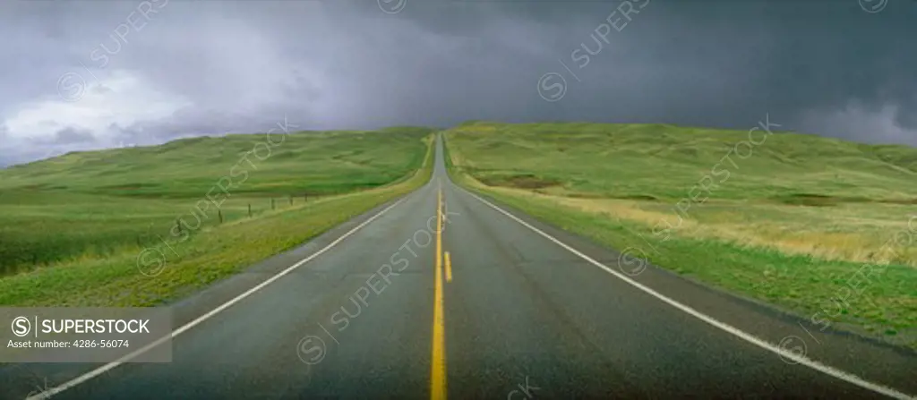 Panoramic view of a two-lane road disappearing into the horizon with cloudy sky, Montana.