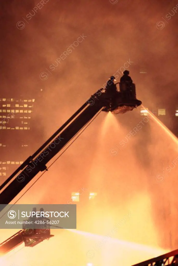 New York City firefighters dousing a blaze from a ladder.  